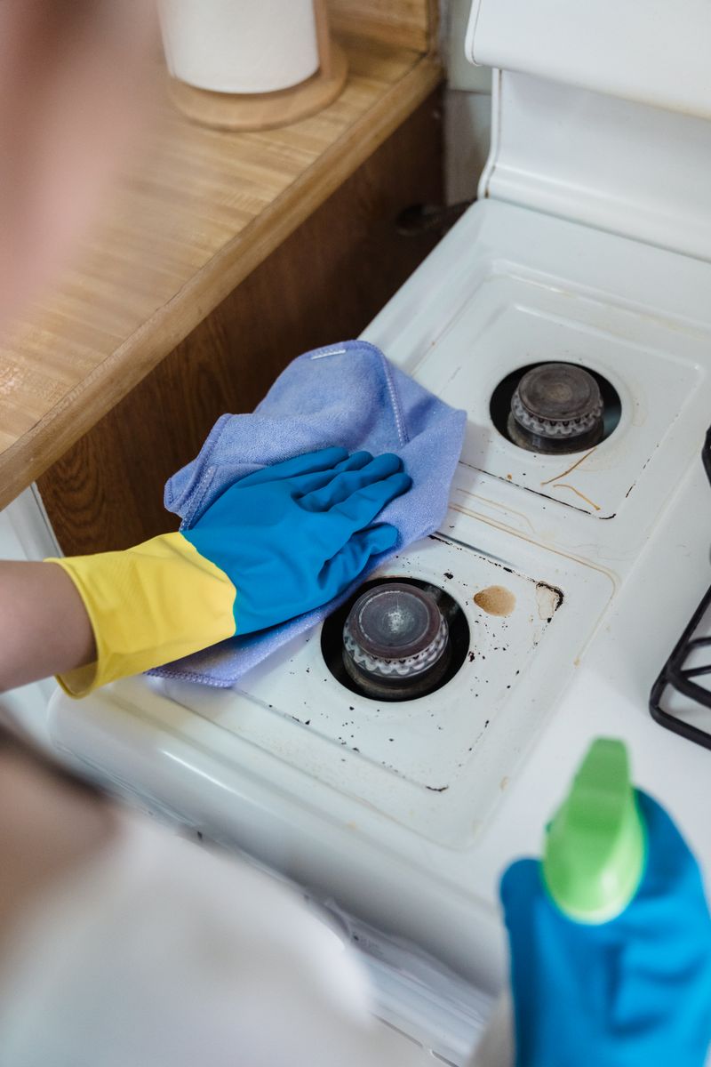 Professional cleaner in rubber gloves thoroughly cleaning kitchen appliance
